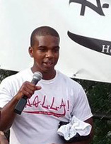 Photo of Cory Greene with a HOLLA t-shirt on speaking into a microphone in front of a HOLLA banner