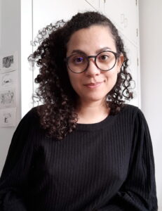 Profile photo of Oriana Mejías Martínez in front of a white wall with small black and white notes or drawings. 