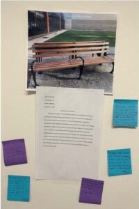 Photo of a brown park bench with a page of printed text underneath on white wall surrounded by blue and purple sticky notes.
