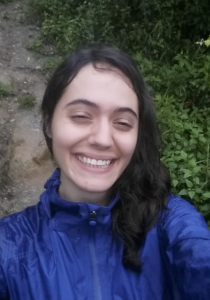 Photo of Miranda smiling in a blue jacket, with dirt and leaves behind her
